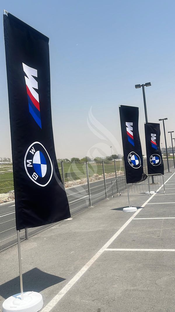 BMW flags on stands in a parking lot with a clear sky.