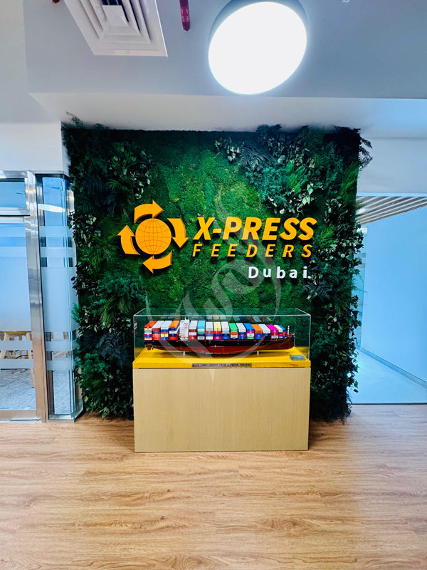 Display case with colorful items in front of a green wall featuring X-Press Feeders Dubai logo.