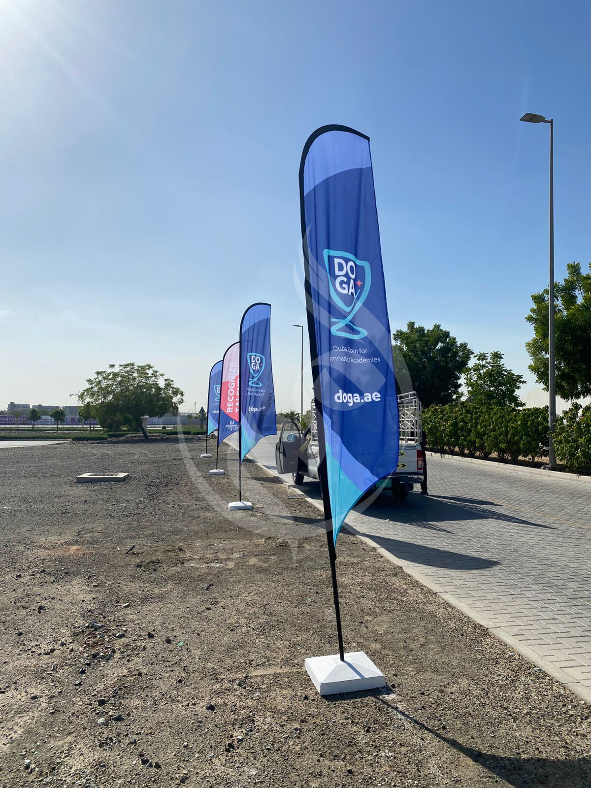 Blue promotional flags with a logo on a paved road under a clear sky.